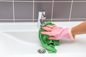 In the bathroom, ceramic sink, tiles and water tap washing and polishing. Maid or housewife cleans house. General cleaning or regular wash up.