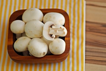 White mushroom champignon in wooden bowl on yellow napkin on a wooden table ready for healthy recipes.