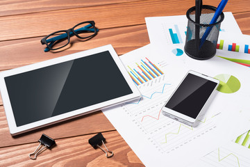 Office desk with tablet, smart phone and charts. Close up