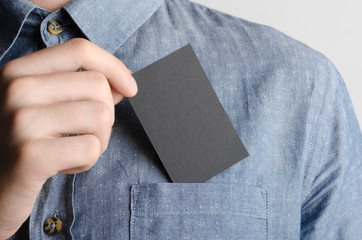 Black Business Card Mock-Up (85x55mm) - Man in a chambray shirt holding a black card on a gray background.