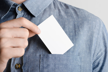 Business Card Mock-Up (85x55mm) - Man in a denim shirt holding a blank card on a gray background.