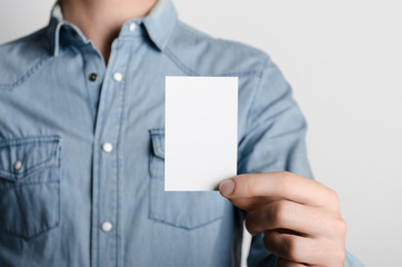Business Card Mock-Up (85x55mm) - Man in a denim shirt holding a blank card on a gray background.