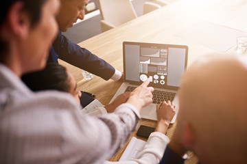 Group of four people pointing to and analysing graphs and charts all displayed on a notebook in front of them to determine performance goals for the next year as a group.