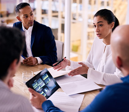 square image of confident young female corporate executive busy giving an explanation for her proposal to expand the firm with one other member looking at financial graphs on his tablet.
