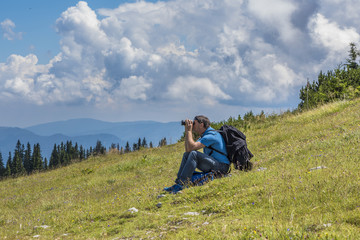 Naklejka na ściany i meble Male Hiker sitting, looking through a binocular on the Rax mountain Austria