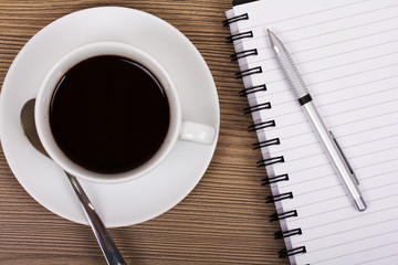 Cup of black coffee and notebook on wooden surface
