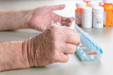 Elderly man sorting daily medication into a pill box.