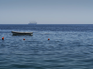 Small boat and a big sailing vessel on blue sea.