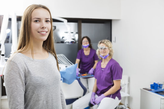 Smiling Female Patient With Dentists Working In Background