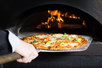 Foto auf Acrylglas Pizzeria Heiße Pizza wird aus der heißen Slove entfernt, wo sie gebacken wurde. Kochen Sie mit einer speziellen Schaufel, um sie zu entfernen. Dieses Restaurant verfügt über einen speziellen Holzofen.