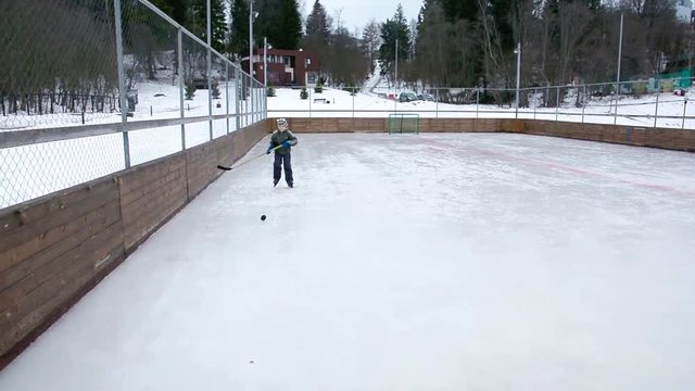 Little boy learns to play hockey at winter day on ice rink