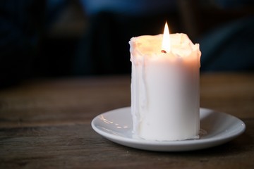 White candle on a white plate standing on a dark wooden table
