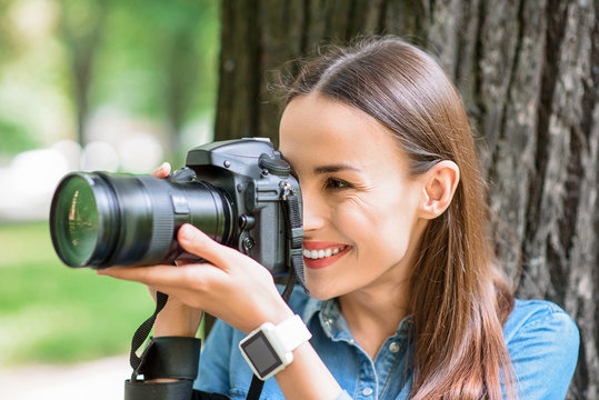 Cheerful young woman photographing in park