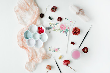 Workspace. Pink and red roses painted with watercolor, paintbrush and roses on white wooden background. Overhead view. Flat lay, top view