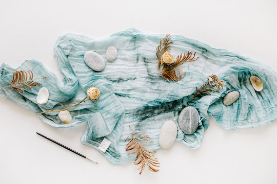 blue textile with stones, dry rose and branches on white background. flat lay, top view