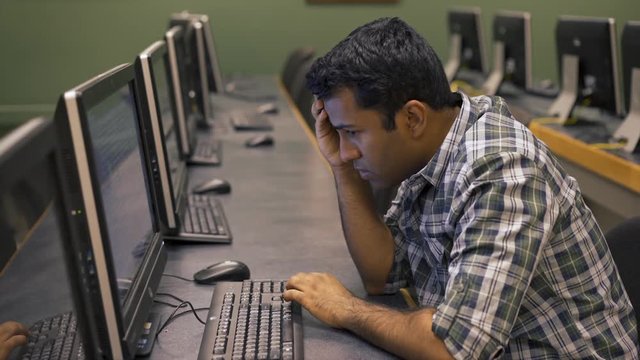 Man in computer lab of college campus looks frustrated while using pc.