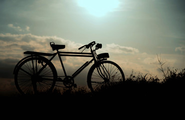 Fototapeta na wymiar silhouette of a retro bicycle. parked in a meadow in evening, th