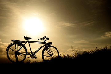 Fototapeta na wymiar silhouette of a retro bicycle. parked in a meadow in evening, th