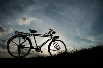 Obraz premium silhouette of a retro bicycle. parked in a meadow in evening, th