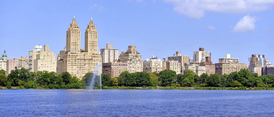 Central Park reservoir with fountain with Upper West Side skyline and blue sky with clouds,...