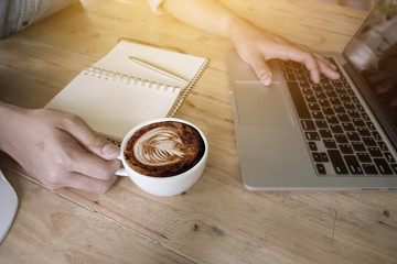 Business man holding a cup of coffee and using laptop, notpad on