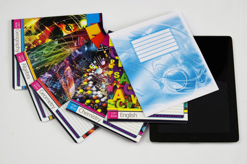 On the table are copybooks for different school subjects and the electronic tablet.