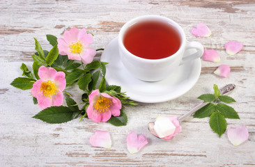 Cup of tea and wild rose flower on old rustic wooden background