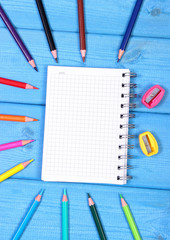 Colorful crayons, sharpener and notepad on blue boards, school accessories, copy space for text