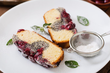 Cherry poppy seed cake dusted with powdered sugar on a wooden table