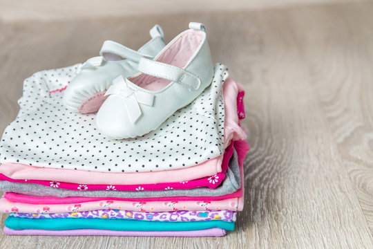 Folded pink and white bodysuit with shoes on it on grey wooden background. diaper for newborn girl. Stack of infant clothing. Child outfit. Copy space.