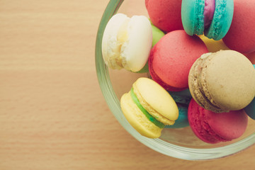 Colorful france macarons in glass cup on wooden background.