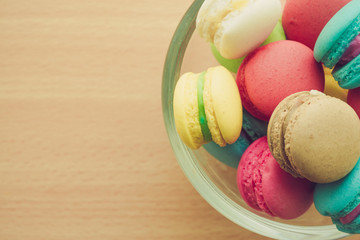 Colorful france macarons in glass cup on wooden background.