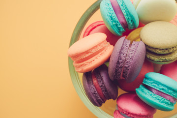 Colorful france macarons in glass cup on yellow background.