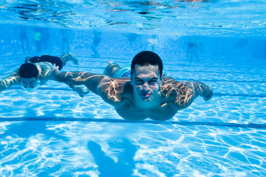 Underwater fun. Two young handsome men swimming underwater and diving in the swimming poll. Sport and leisure.