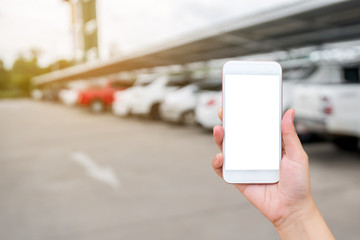 Woman hand showing smart phone on blurred car in parking lot