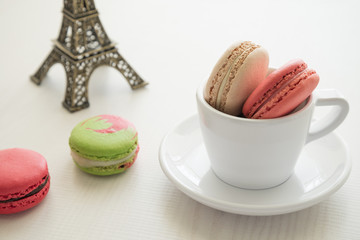 Colorful france macarons and cup on white wooden background.
