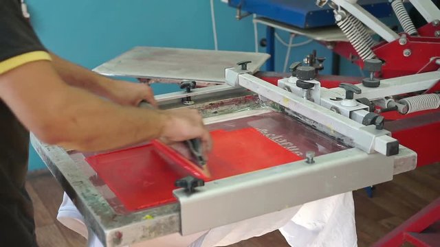 Screen printing manufacturing on t-shirts. Worker print an image on fabric on a hand bench