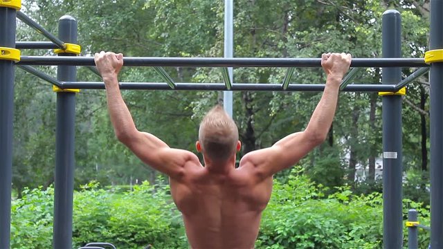 Athletic man doing pull ups on horizontal bar in City Park. rear view. Workout.
