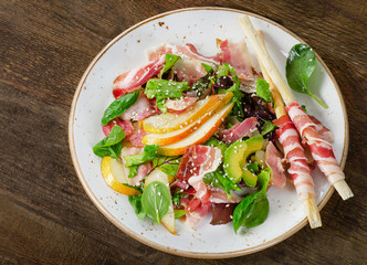 Fresh mixed salad with pancetta and pear on a wooden table.