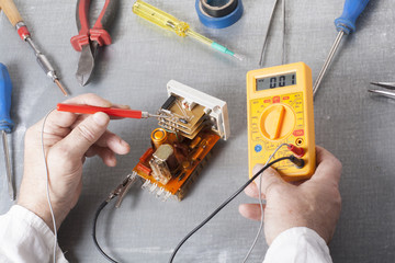 Hand of electrician with multimeter probe at  electrical switchgear cabinet. Engineering tools