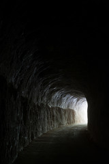 Dark road in a natural rocky tunnel and the light of the exit