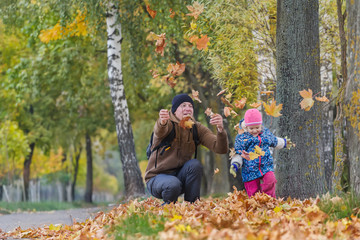 Happy father with little daughter tossing up yellow autumn leaves in park outdoors
