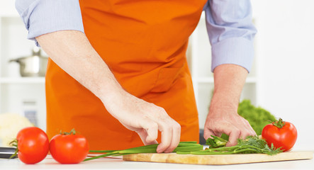 Mid section of a man cutting the chop of green onions in the kitchen at home.