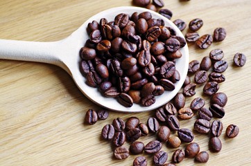 Coffee beans on a wooden spoon on a rustic wooden background.