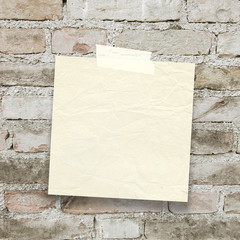 Close-up of one blank square old paper sheet frame with adhesive tape on old brick wall background