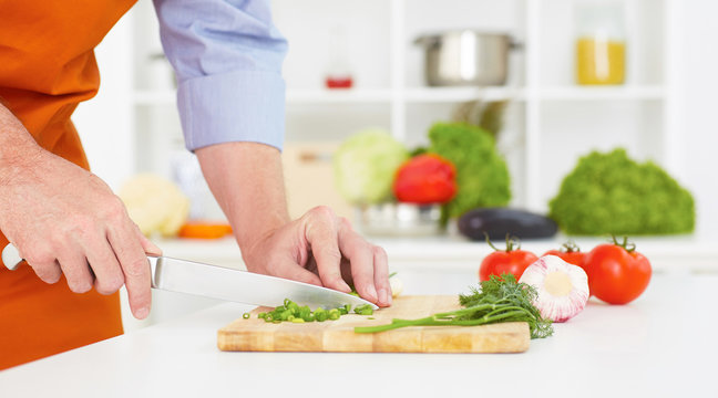 Close-up of man's hands chopping onion on cutting board.