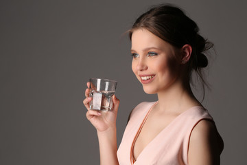 Smiling model with glass of water. Close up. Gray background