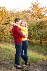 Fototapeta premium Love, relationship, season, friendship and people concept - happy man and woman enjoying golden autumn fall season with paper coffee cups in the park. Young couple drinking hot cofee or tea.