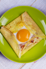 Egg on pancake with bacon and cheese in green plate. View from above, top studio shot