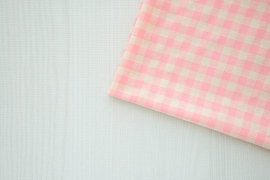 Pink gingham tablecloth on white wooden table background